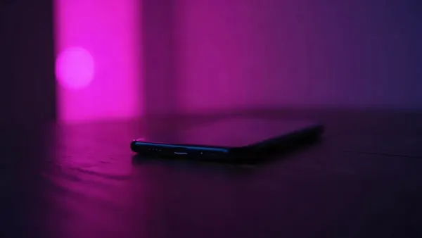 Smartphone op een donkere houten tafel, omringd door paarse en roze reflecties (illustratie bij het artikel)